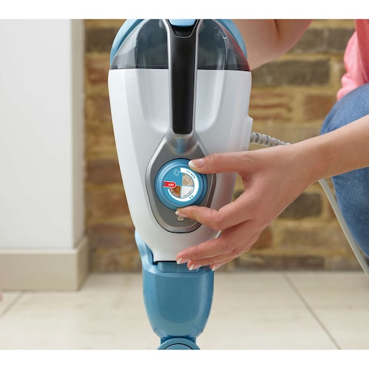 BLACKDECKER FSMH1321JSM steam mop close-up, hand adjusting control dial, white and blue design, indoor setting.