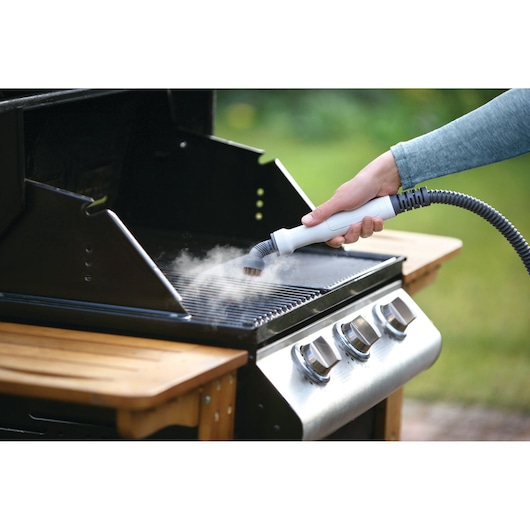 BLACKDECKER FSMH1321JSM steam cleaner cleaning grill, hand holding nozzle with steam on barbecue.