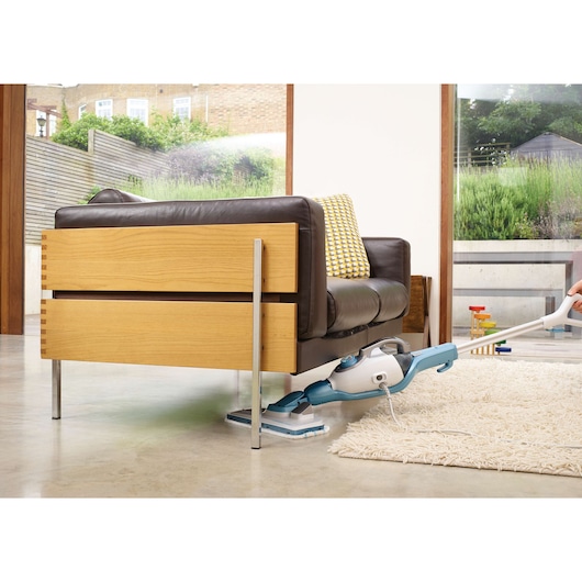 BLACKDECKER FSMH1321J steam mop cleaning under sofa on concrete floor, side angle.