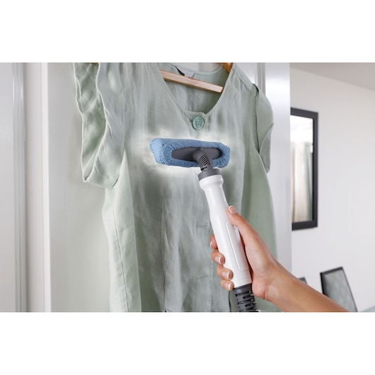 BLACKDECKER FSMH1351SM handheld steam cleaner used to freshen a light green shirt hung on a wooden hanger.
