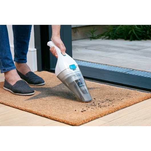 BLACKDECKER FSMH13ENVC1 handheld vacuum cleaning dirt from a brown doormat near an open door.
