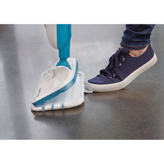 Close-up of a person using their foot to attach a white cleaning pad to a BLUE and white BLACK+DECKER steam mop on a hard floor.