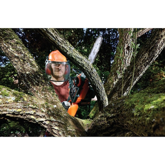 BLACKDECKER GKC3630L20 chainsaw used outdoors for tree trimming, person wearing safety gear.