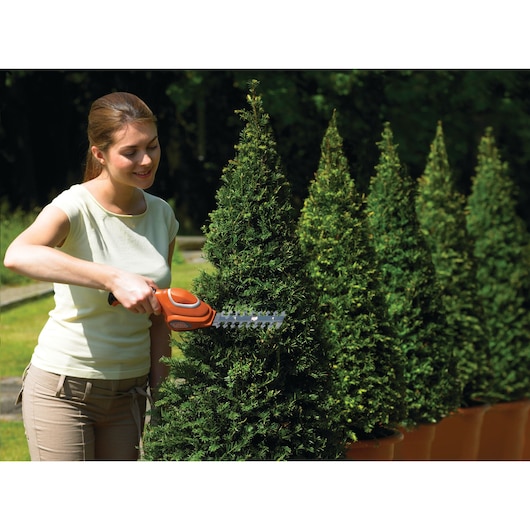 BLACKDECKER GSL700 cordless shrub shear being used to trim potted topiary outdoors.