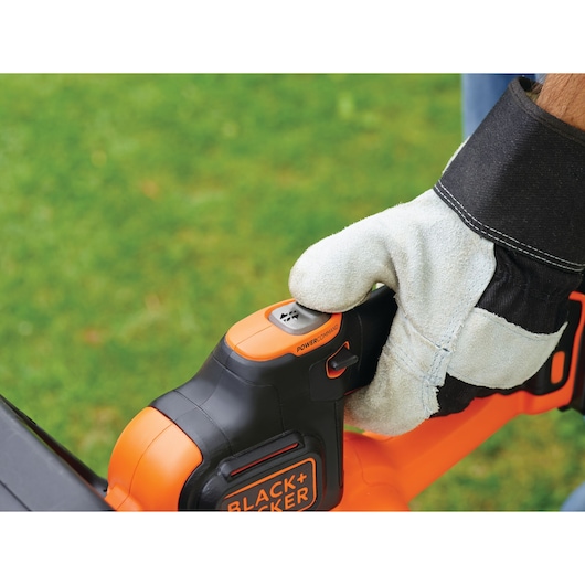 Photo of BLACKDECKER GTC18502PC hedge trimmer handle with glove pressing Powercommand button outdoors.