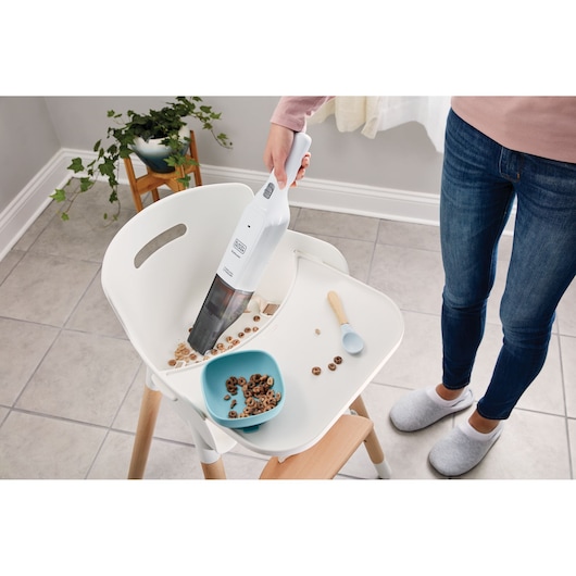 BLACKDECKER HLVC315B11 handheld vacuum cleaning cereal from a white high chair tray in a kitchen.