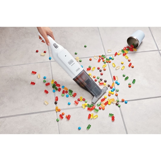 BLACKDECKER HLVC315B11 handheld vacuum cleaning spilled candy from tile floor, top view.