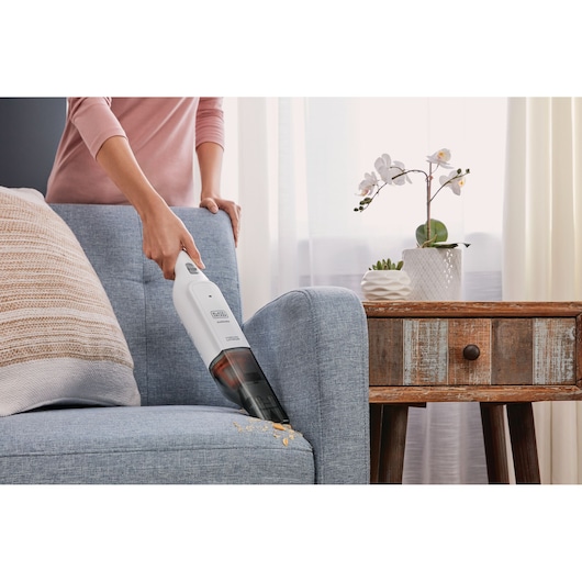 BLACKDECKER HLVC315B11 handheld vacuum cleaning crumbs from a blue sofa beside a wooden side table.