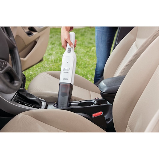BLACKDECKER HLVC315J11 handheld vacuum cleaning car interior between beige seats.