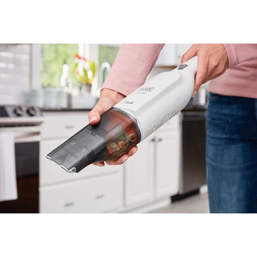 Photo of BLACK+DECKER HLVC315J11 handheld vacuum cleaning up food debris in a kitchen.