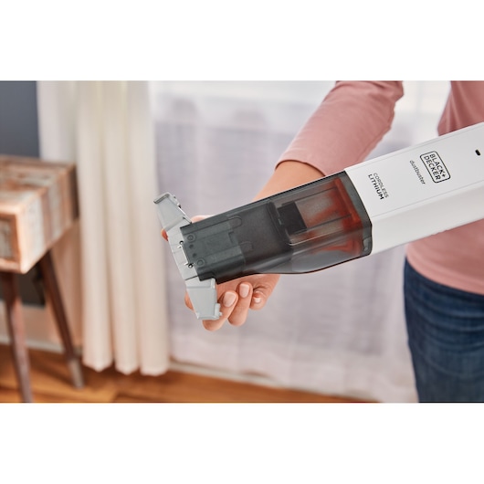Photo of BLACK+DECKER HLVC315J11 cordless handheld vacuum being emptied, held by a person indoors.