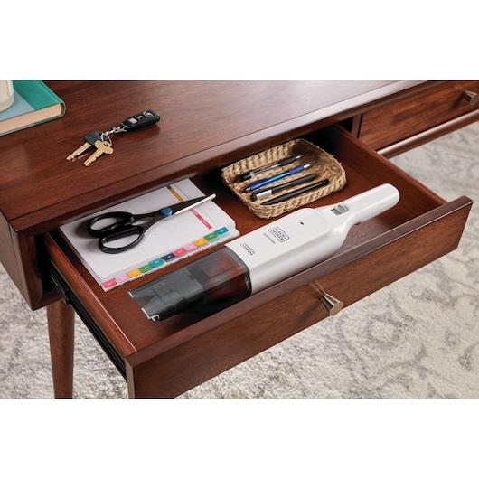 Photo of BLACKDECKER HLVC315J11 handheld vacuum in a wooden desk drawer with office supplies.