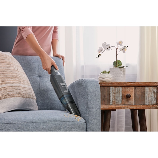 BLACK+DECKER HLVC320B11 handheld vacuum cleaning sofa crumbs in living room.