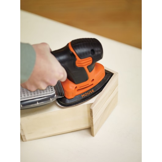 A hand using a BLACK+DECKER KA2000AT Mouse sander to smooth a wooden box corner.