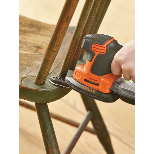 A person is using a BLACK+DECKER Mouse sander to sand the curved edge of a wooden chair.