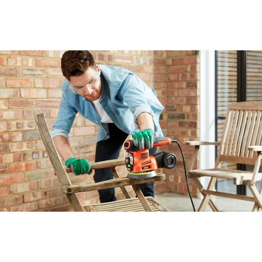 BLACKDECKER KA280LSA2 multi-sander in use sanding a wooden chair, product held by gloved hands.