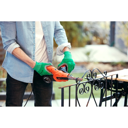 Person using BLACKDECKER KA900E power file sander on decorative metal railing outdoors.