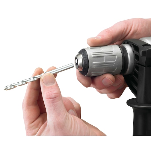 Photo of hands inserting a drill bit into BLACKDECKER KR1102K power drill chuck, close-up, white background.