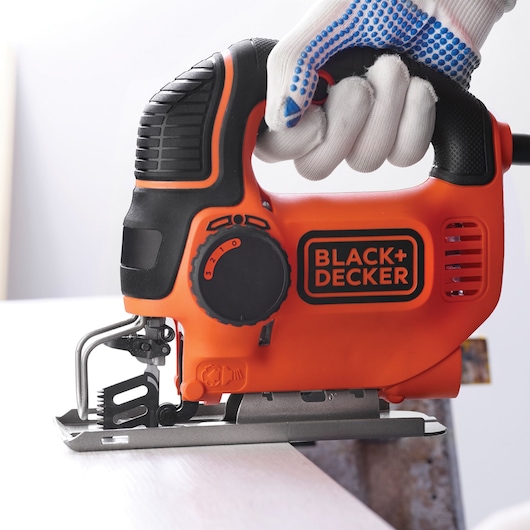 Photo of BLACK+DECKER KS901PEKA5 orange jigsaw held by a gloved hand cutting wood.
