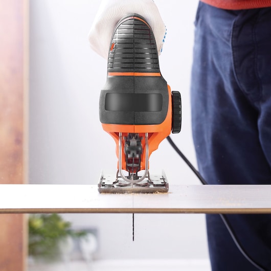 BLACKDECKER KS901PEKA5 jigsaw in use, cutting wood, front angle, orange and black tool held with glove.