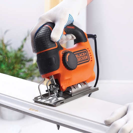 Photo of BLACKDECKER KS901PEKA5 jigsaw in use, orange and black, cutting wood, close-up with gloved hand.