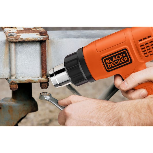 BLACK+DECKER KX1650 heat gun in use on a rusted metal bolt with wrench, close-up view.