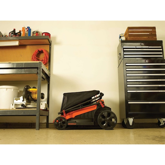 BLACKDECKER LM2000 lawn mower folded for storage, side view, in a garage setting next to shelves and a tool chest.