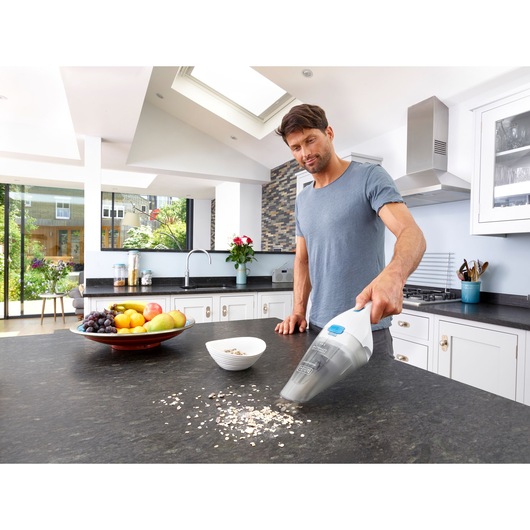 BLACKDECKER NVC115JL handheld vacuum cleaning kitchen counter near bowl of oats and fruit plate.
