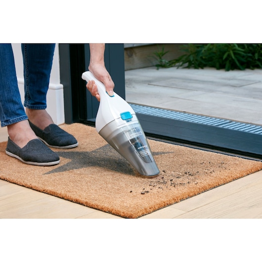 BLACKDECKER NVC115JL handheld vacuum cleaner used to clean dirt on a doormat indoors.