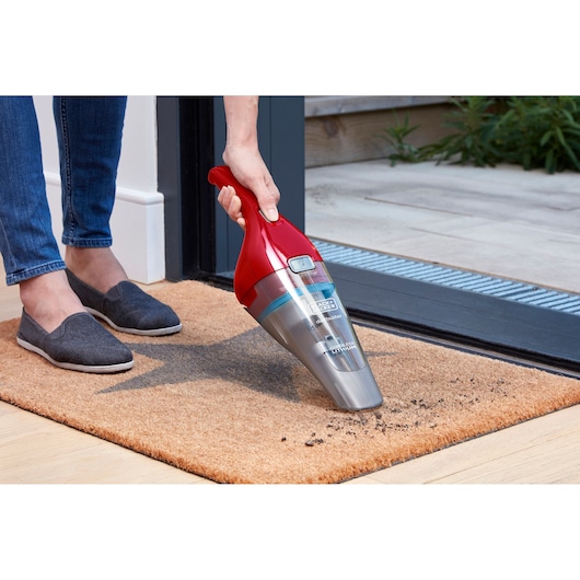 BLACKDECKER NVC115WAR handheld vacuum cleaner used on a doormat near an open door.