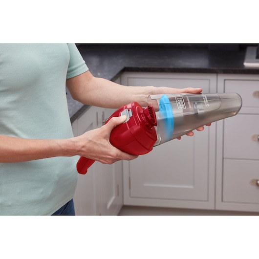 Photo of a person removing the dust container from a BLACK+DECKER handheld vacuum NVC115WAR in a kitchen.
