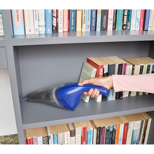 BLACKDECKER NVC115WA handheld vacuum cleaning gray bookshelf near books, photo from side angle.
