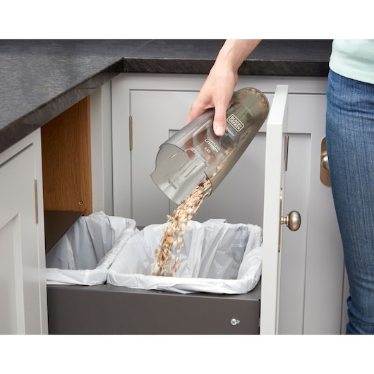 Photo of BLACKDECKER NVC115WA handheld vacuum canister being emptied into a kitchen trash bin.