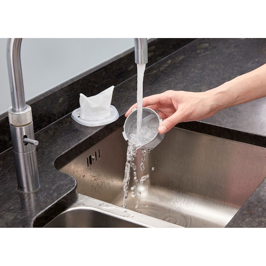BLACKDECKER NVC115W vacuum filter being rinsed under a kitchen faucet over a stainless steel sink.