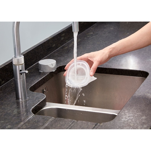 Photo of BLACKDECKER NVC220WC vacuum filter being rinsed with water in a kitchen sink.