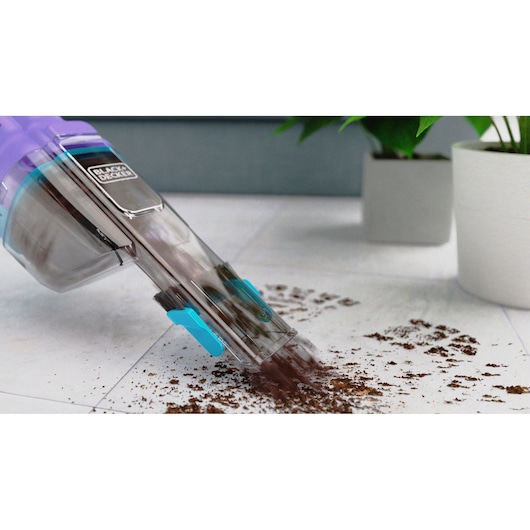 BLACK+DECKER NVD220BP handheld vacuum cleaning dirt from white floor with potted plants in background.
