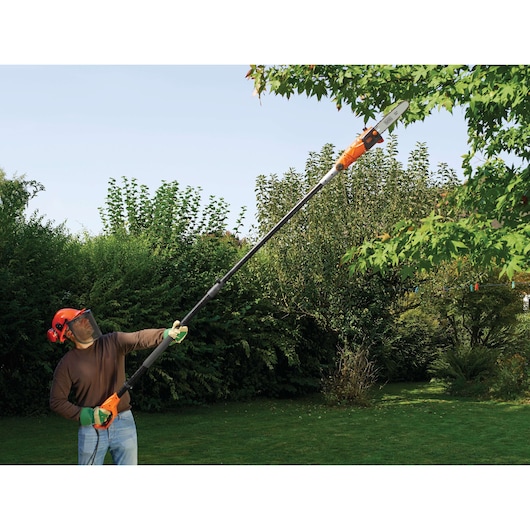 BLACKDECKER PS7525 pole saw used for trimming tree branches outdoors in a garden setting.