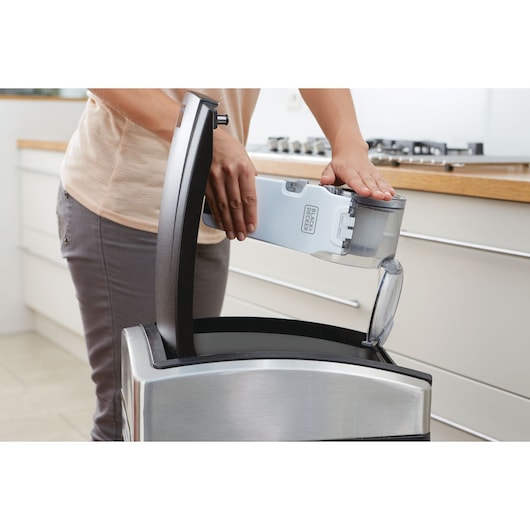 Person emptying BLACKDECKER PV1820L handheld vacuum dust container into kitchen trash bin.