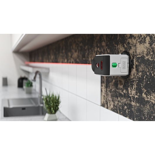 BLACKDECKER REVBDLL100 laser level tool mounted on kitchen wall, projecting red guideline above tiles, side angle