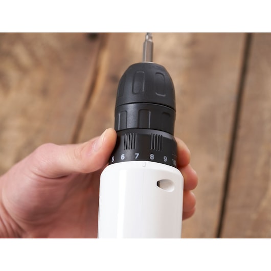 Close-up photo of BLACKDECKER REVDD12C cordless drill showing hand adjusting torque settings, wood background.