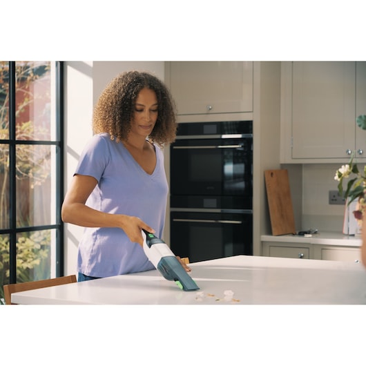 Photo of a person using a BLACKDECKER REVHV8CA handheld vacuum cleaner to clean crumbs from a kitchen counter.