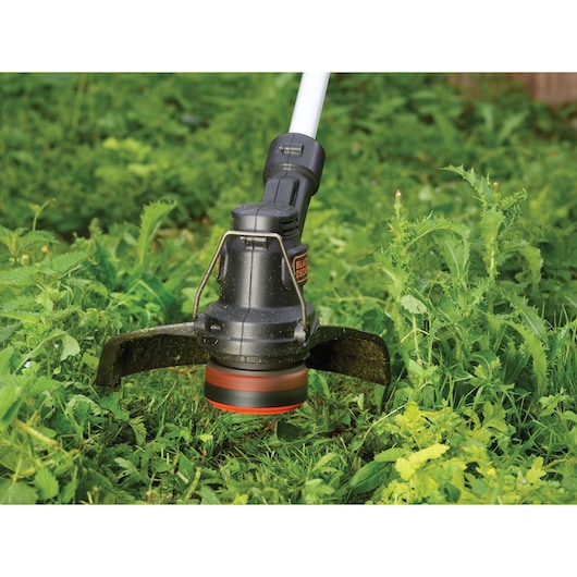 Close-up view of a BLACK+DECKER string trimmer cutting through green grass and weeds.