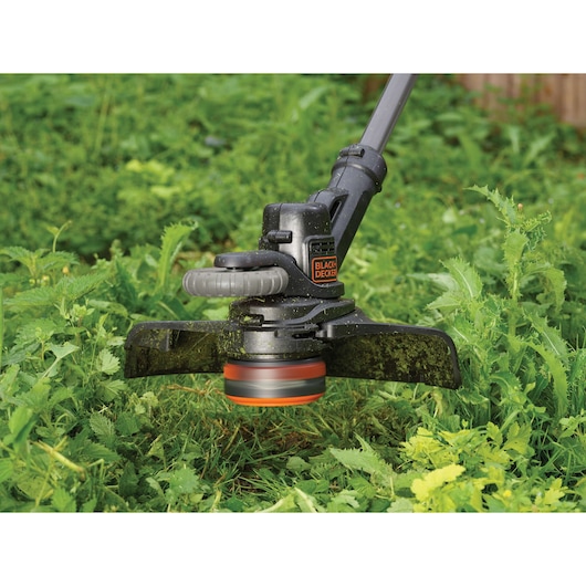 BLACKDECKER STC1840EPC grass trimmer in use, close-up showing cutting head trimming green weeds.