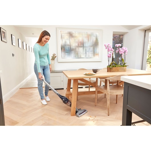BLACKDECKER SVB520JW cordless stick vacuum in use cleaning crumbs on wooden floor near dining table.